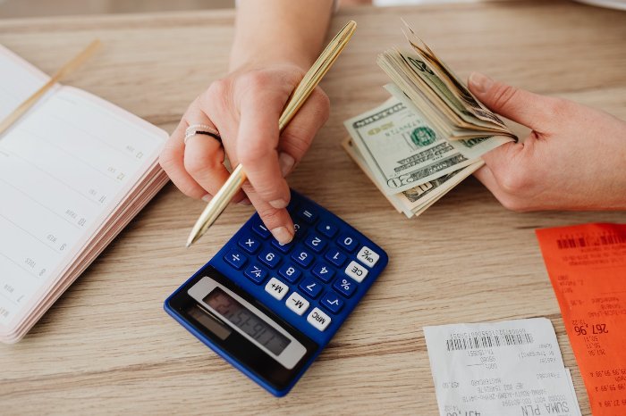 Person with money typing into a calculator.
